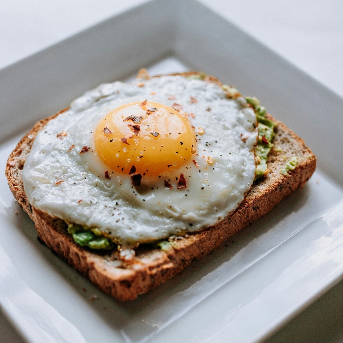 Fried egg on avocado toast on a white plate