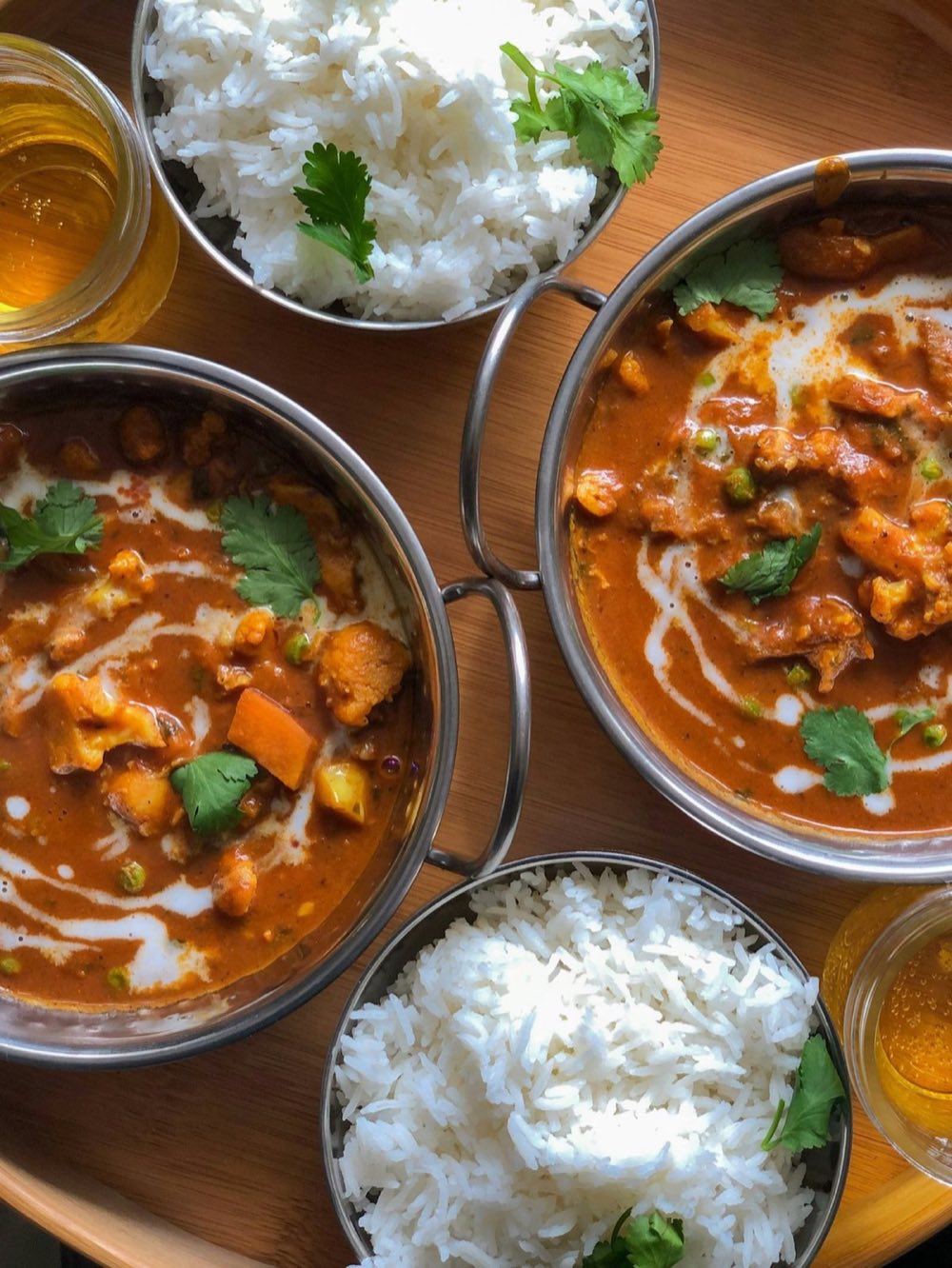 Two bowls of curry with rice and cilantro on a wooden tray