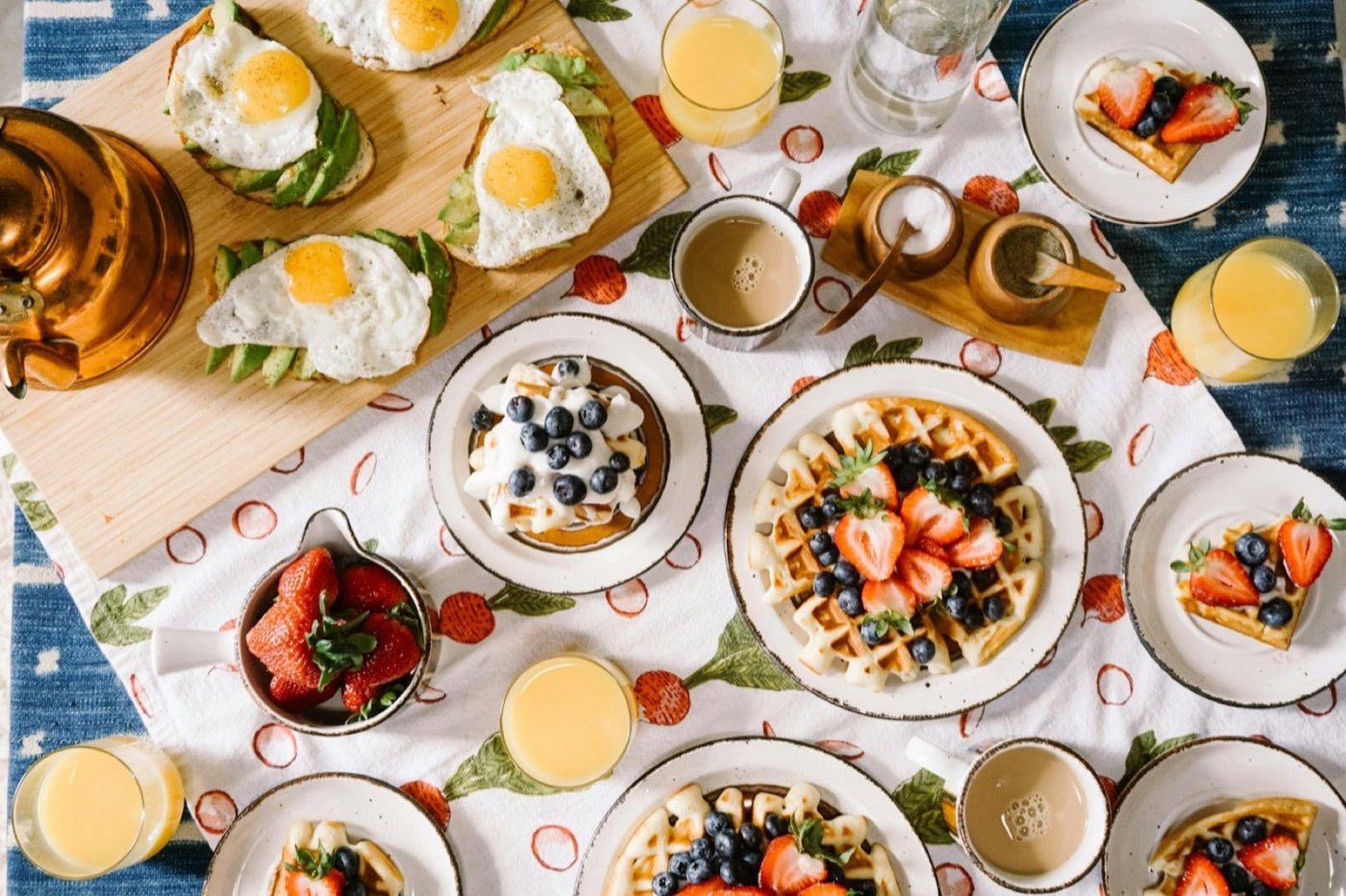 Bright breakfast spread with waffles, eggs on toast, fruit and juice