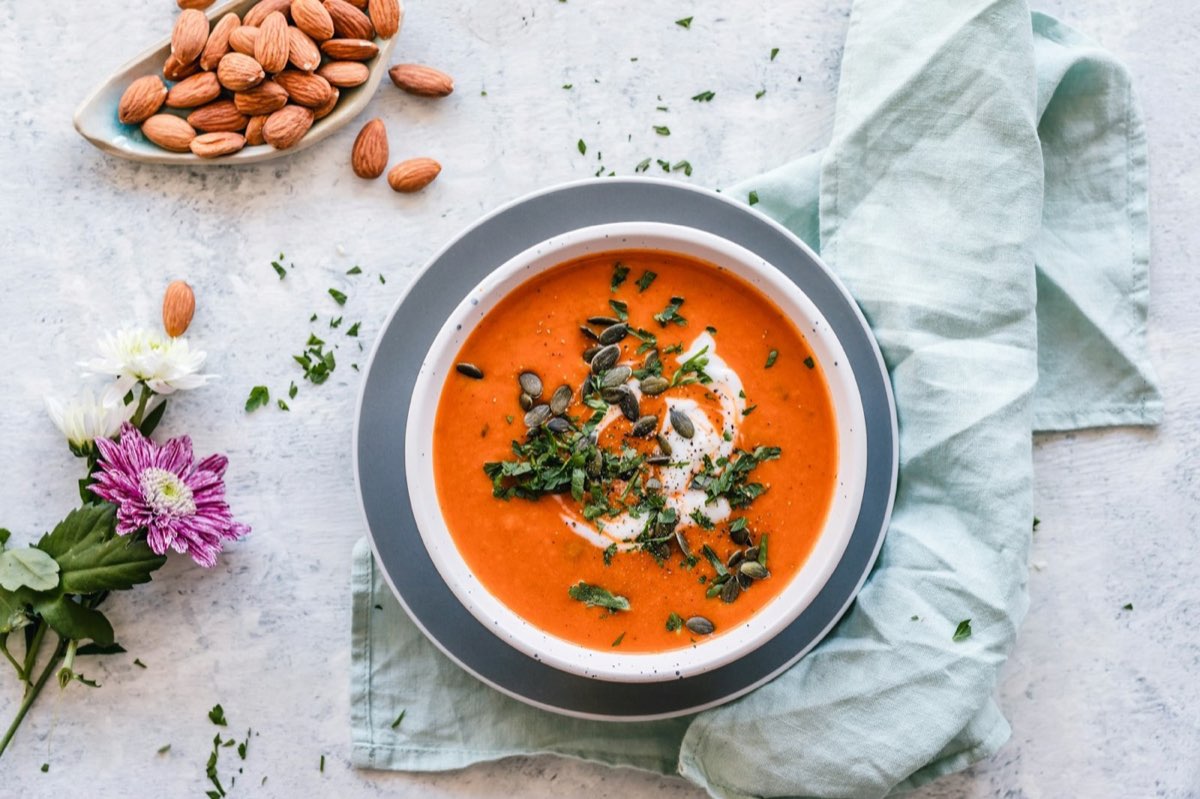 Bowl of tomato soup topped with herbs and seeds